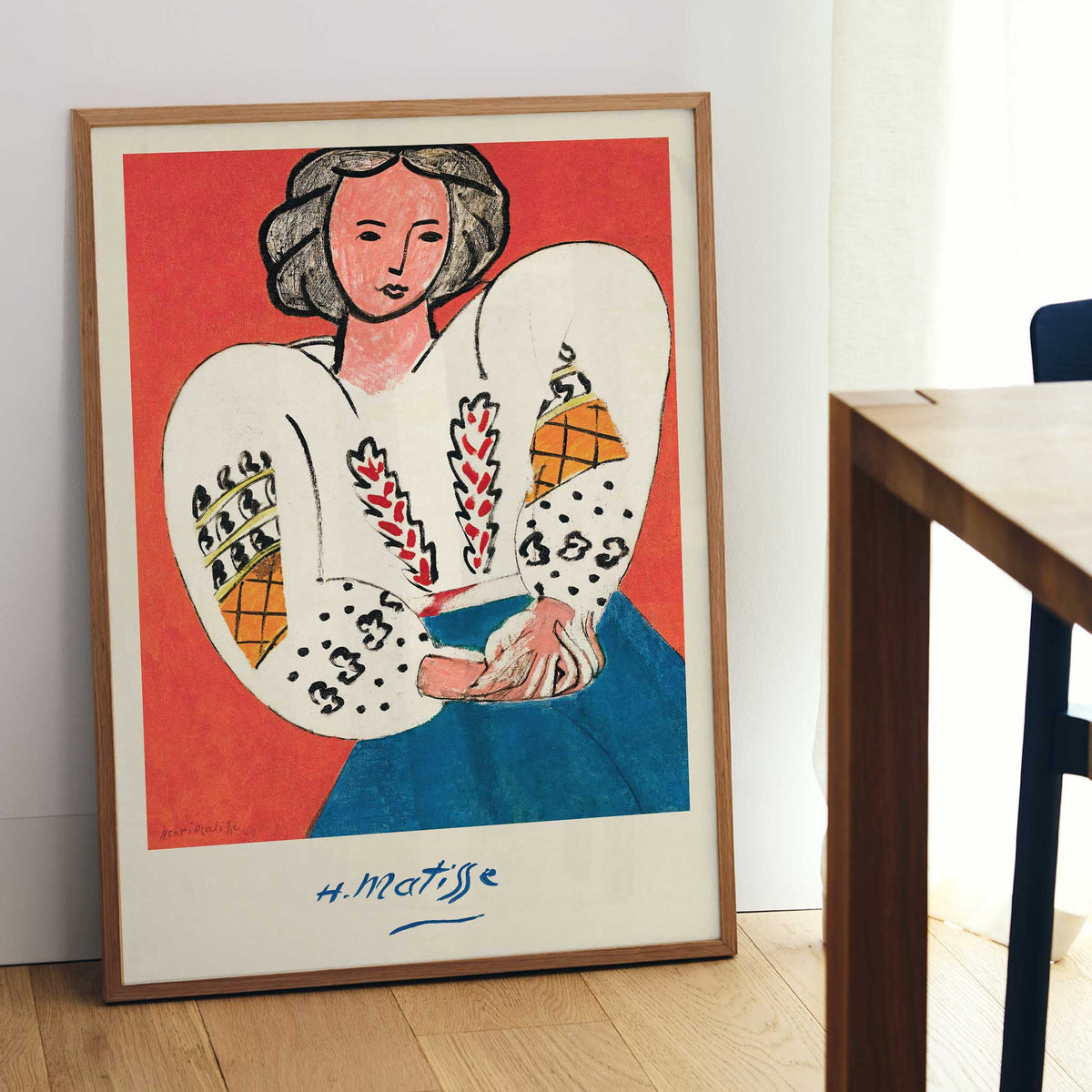 Henri Matisse The Romanian Blouse poster with woman in embroidered white blouse and blue skirt against red ground, with wooden magnetic frame on white background