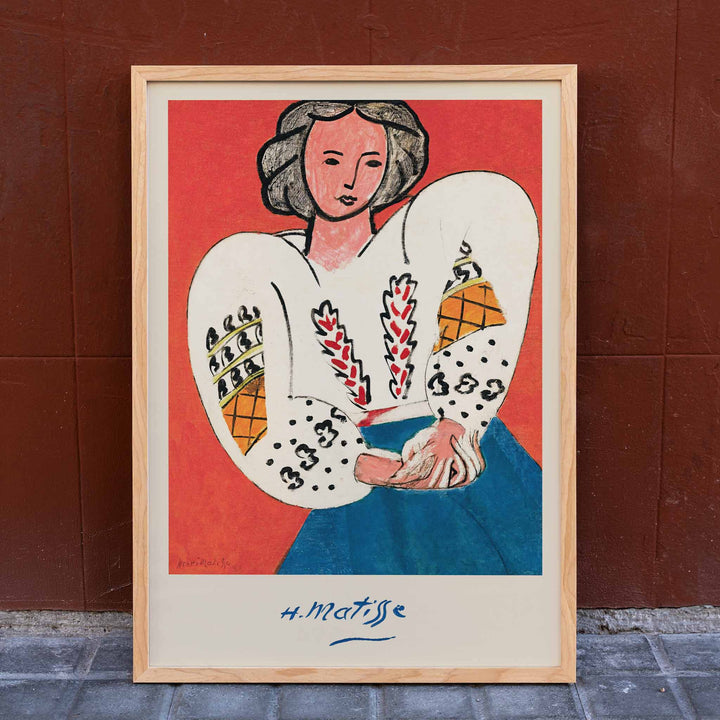 Henri Matisse The Romanian Blouse poster with woman in embroidered white blouse and blue skirt against red ground, framed and displayed in home decor