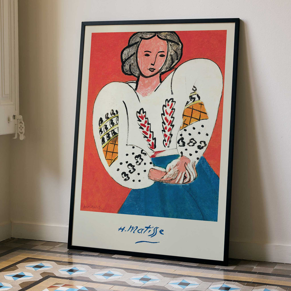 Henri Matisse The Romanian Blouse poster with woman in embroidered white blouse and blue skirt against red ground, framed and displayed in modern living room decor