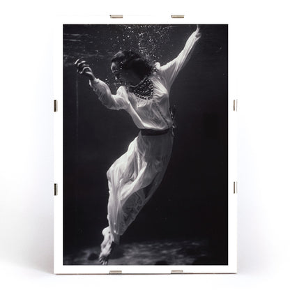 Black and white artwork of a fashion model floating underwater in dolphin tank Marineland Florida by Toni Frissell, framed and displayed in modern living room decor